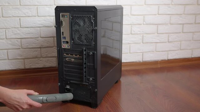 Technician cleaning pc tower case with vacuum cleaner. Technician's hands cleaning a black desktop computer case using a vacuum cleaner to remove dust from the vents and power supply
