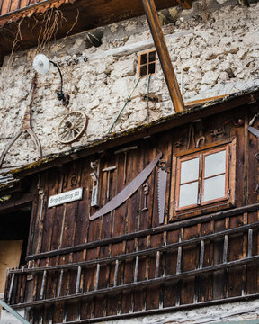 View of a rustic wooden wall decorated with antique tools, including saws and a wooden wheel, set against a stone masonry facade in Hallstatt, Upper Austria, Austria.