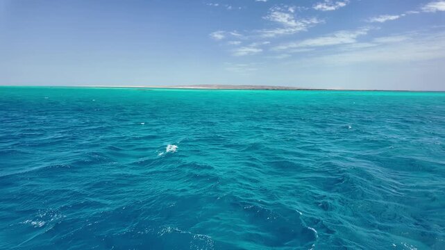 Panoramic view of vivid turquoise and deep blue waters of the Red Sea with a remote sandy desert island near Hurghada, Egypt. Gentle waves, clear tropical sea and an almost empty island coastline unde