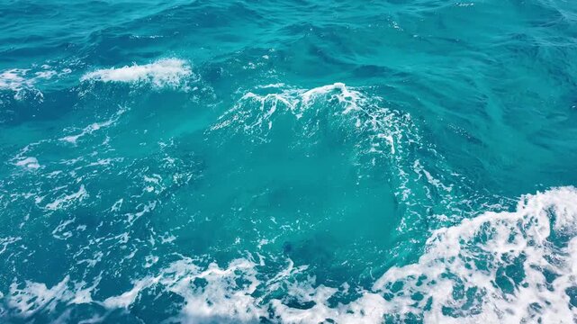 Clear blue water churns with white foam. Waves roll forward, sparkling under sunlight. Ocean's movement feels alive and wild. Perfect for travel or adventure backgrounds.