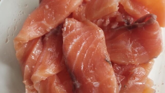 Fresh raw salmon fillets, sliced and lightly seasoned with salt, rest inside a clear glass dish in a close-up macro shot. For culinary commercials, seafood recipe tutorials, healthy eating promotions.