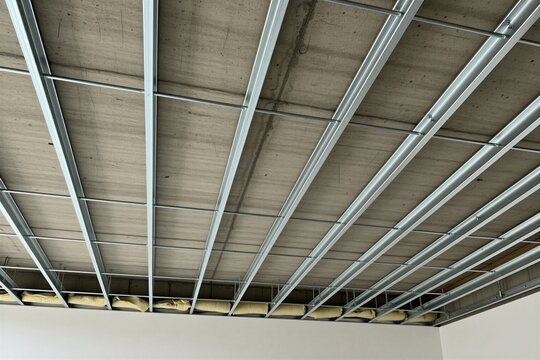 Metal ceiling frame structure attached to concrete slab inside room. Steel profiles create grid for drywall installation during building renovation work. Pro crew builds suspended ceiling system in
