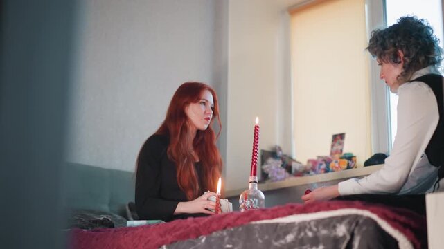 Candlelit counsel between white redhead woman and white man, intimate bedside exchange with cards and single tall candle, woman sharing doubts while reader listens, warm light and candid emotional