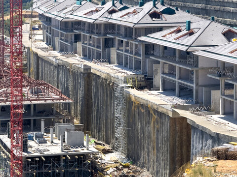 View of a modern residential construction site featuring multi-story houses built along a high concrete retaining wall with scaffolding and a red crane in Avcilar, Istanbul, Turkey.