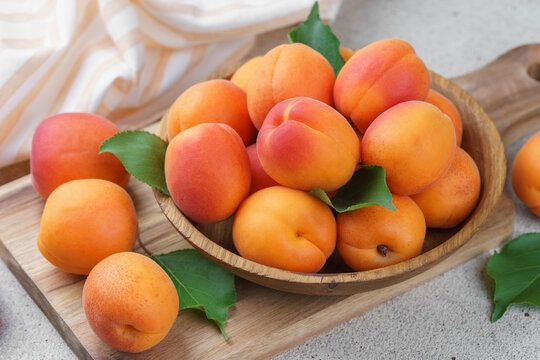 Close up of fresh ripe apricots in rustic wooden bowl with green leaves on gray textured background. Healthy seasonal summer fruit, healthy food, nutrition, ingredient for cooking and desserts
