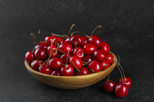 Fresh ripe sweet cherries in rustic wooden bowl on black stone textured background with copy space for text. Juicy organic summer fruit, red berries, healthy seasonal food, farm harvest
