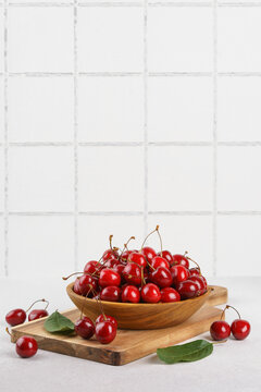 Fresh ripe sweet cherries in wooden bowl on rustic cutting board with green leaves and linen cloth on white tiled background. Healthy summer fruit, red berries, fresh seasonal harvest, healthy food