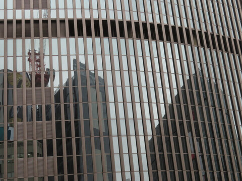View of the modern glass and metal facade of a skyscraper with reflections of surrounding buildings and a construction crane in Tokyo, Tokyo, Japan.