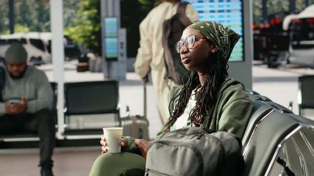 Smiling woman holds a coffee cup while waiting in a bus terminal, enjoying a refreshment before her coach journey as an African American female traveler preparing for intercity travel.