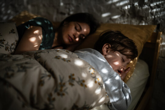 Mother and son sleeping peacefully in bed with sunlight