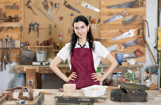 Happy young woman in pinafore standing in taller workroom full of tools