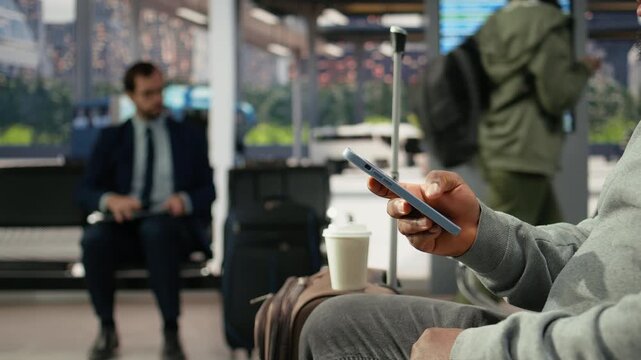 Traveler uses a smartphone app in a bus station to plan a route connection, texting on a mobile phone in the coach waiting area before a long-distance trip.