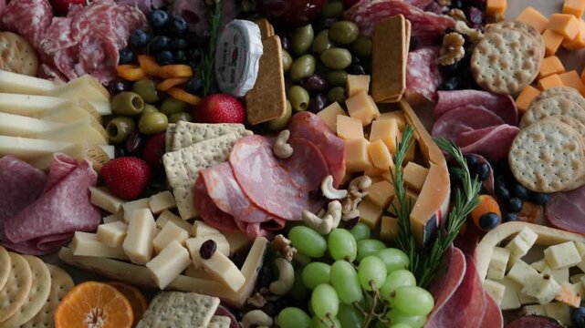 Overhead close-up of a charcuterie board with cured meats, assorted cheeses, crackers, olives, grapes, strawberries, blueberries, mandarin orange, dried apricots, nuts and fresh rosemary sprigs
