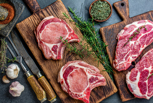 Raw pork cutlet chop for fry on pan with herbs, garlic on wooden boards, slate gray background
