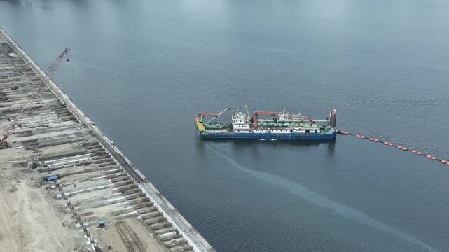Cilincing, Jakarta, Indonesia - 06 August 2026: Aerial view of a dredging vessel operating in the Kali Baru canal near a construction site.