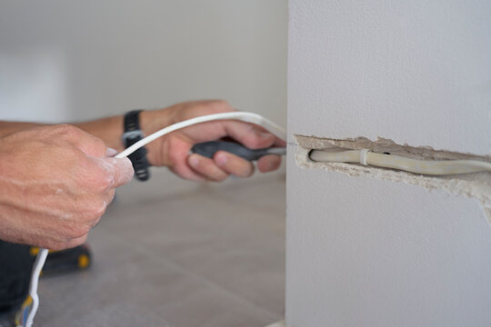 Man pulls electrical cable through a channel cut into an interior wall