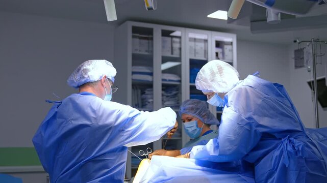 Surgeons and nurse stand near the operating table. Medics work at the surgery on traumatized foot.