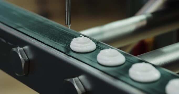 Automated nozzle deposits equal portions of white viscous product onto conveyor. Precision dosing system forms uniform units during factory food production
