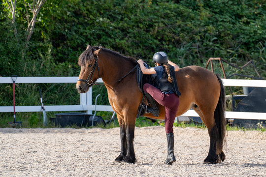 Rider mounting a saddled horse in an outdoor riding arena