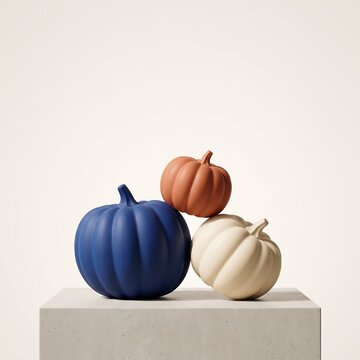 A stack of three decorative pumpkins in blue orange and white colors sitting on a minimalist white pedestal display stand