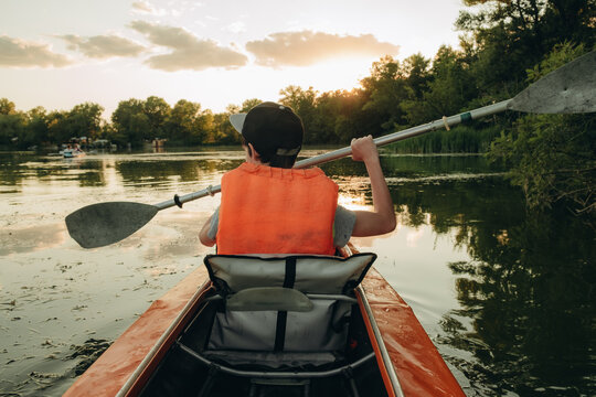 Boy in life jacket kayaking on calm river water during sunny summer day, outdoor active lifestyle and water sport concept