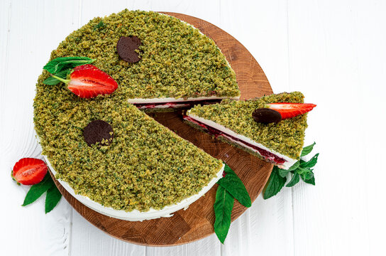 Overhead shot of pistachio berry cake with cut slice. Flat lay view of green dessert decorated with fresh strawberries chocolate and mint.