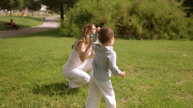 Playful mother and son blowing soap bubbles in the park