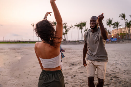 Energetic young people dancing with joy on the sandy beach at sunset, celebrating summer and freedom