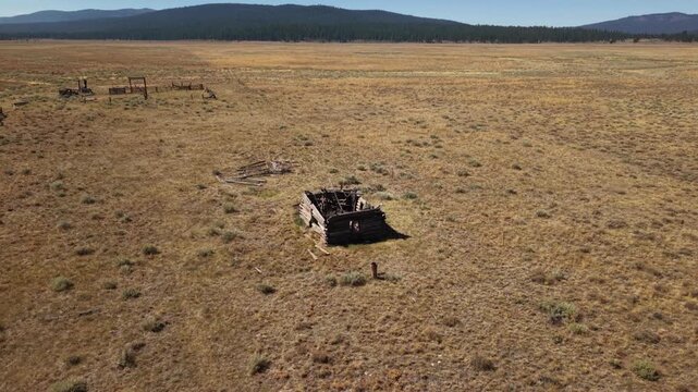Rocket shot drone ascends to reveal abandoned cabin and corral on open Lassen County rangeland, California.