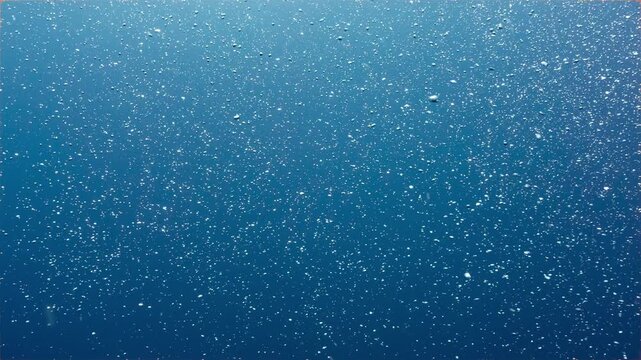 Underwater abstract shot of shimmering bubbles in open blue water	