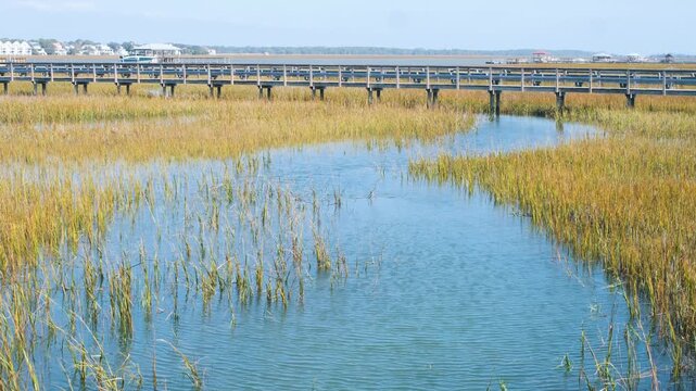 Flowing salt water tidal creek at a very high tide with marsh grass, and a dock boardwalk, 4k, slow motion.