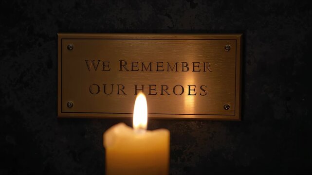 Candle flame illuminating a memorial plaque honoring fallen heroes, symbolizing remembrance, tribute, mourning, gratitude, and patriotic commemoration