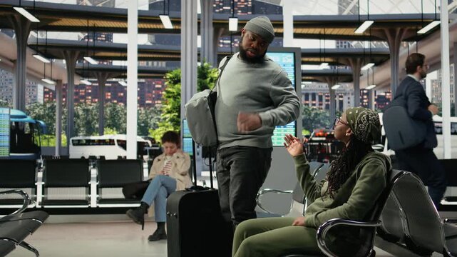 Woman waves goodbye from a bus terminal bench as her companion leaves with a trolley, while a man salutes his friend in a coach station before departure and walks away with luggage.