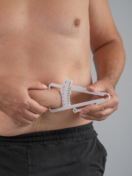 A man measures the amount of subcutaneous fat on his stomach using a caliper.