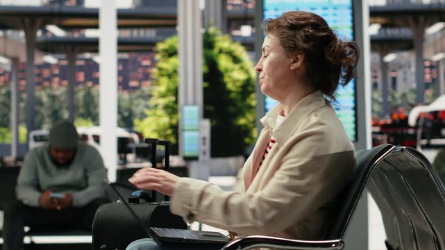 Woman uses a notebook in a bus terminal and texts friends on a smartphone during a long wait, switching between the laptop and mobile phone before departure.
