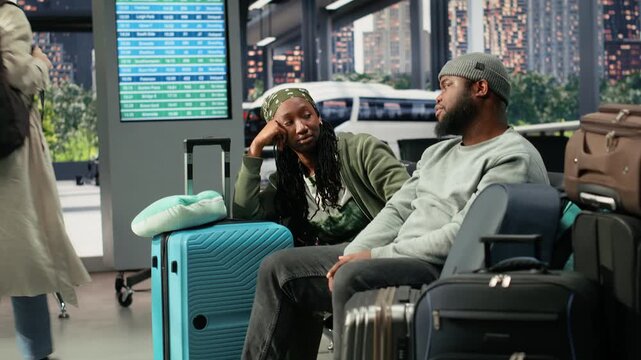 Exhausted travel companions discuss route plans beside a suitcase in a bus station before departure, talking in the shuttle terminal while tired and waiting for their next coach connection.