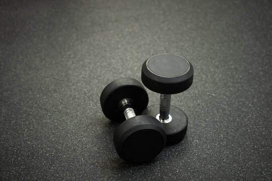 This monochrome photo shows two dumbbells lying on the gym floor, emphasizing the simplicity and purposefulness of training and strength exercises.
