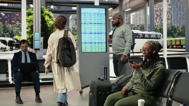 Traveler dictates a voice message on a smartphone in a bus terminal, holding the phone near her mouth and sending an audio message before departure.