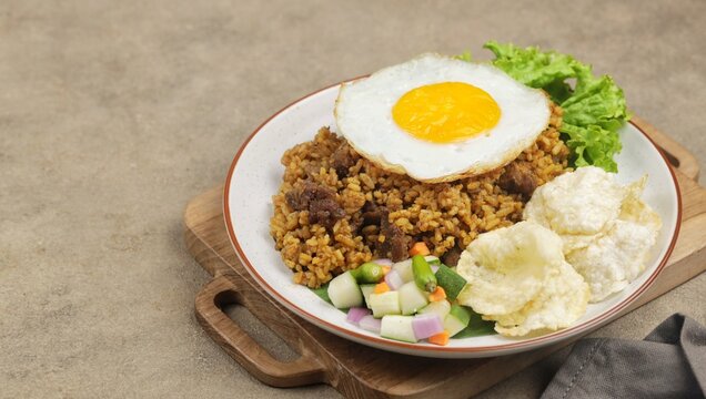 A plate of fried rice with lamb, fried egg, tomato, shrimp crackers, cucumber and lettuce isolated on wooden textured. Nasi Goreng Kambing, indonesian food