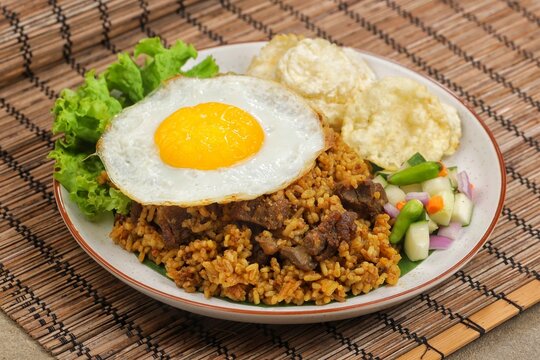 A plate of fried rice with lamb, fried egg, tomato, shrimp crackers, cucumber and lettuce isolated on wooden textured. Nasi Goreng Kambing, indonesian food
