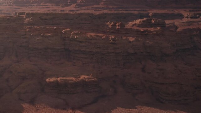 In a canyon, sunlight shines on large red rock formations. The rocks show layers that have been shaped by wind and time. The landscape has shadows and steep cliffs.