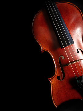 A polished wooden violin against a deep black background, highlighting its elegant curves, strings, bridge, and rich warm tones with dramatic studio lighting and ample copy space.