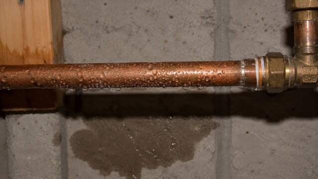 Cold water pipe in residential basement showing beads of condensation and small damp area directly beneath pipe
