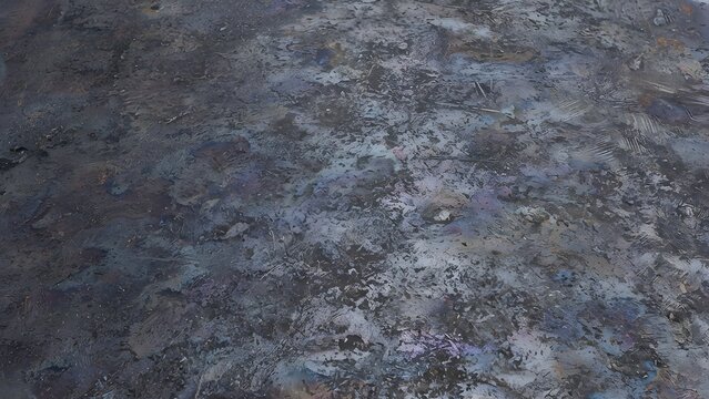 Close-up textured background of dark iridescent oil slick patterns on a metallic surface.