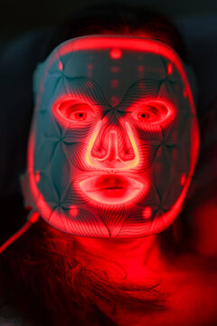 Woman wearing glowing red LED light therapy mask with geometric patterns, illustrating modern skincare technology and futuristic beauty treatment.