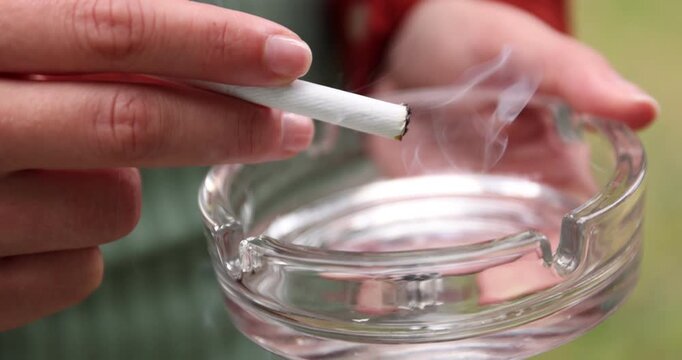 Woman flicking ash from cigarette into ashtray outdoors, closeup. Camera moving in