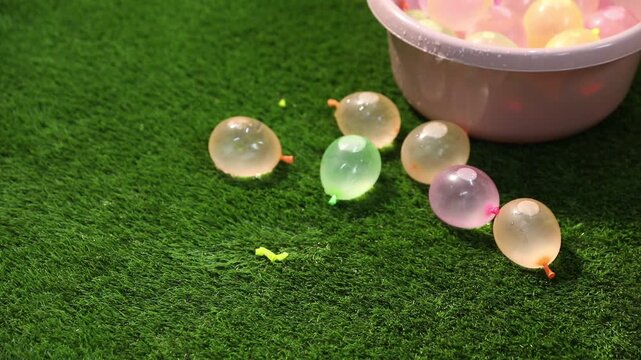 Woman taking water balloon from basin and throwing it onto green grass, closeup