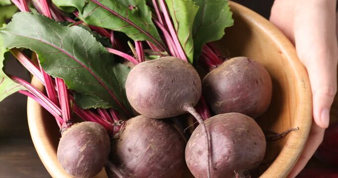Woman showing bowl of fresh young beet with green leaves at table, closeup