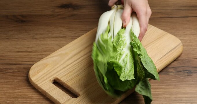 Woman cutting bok choi (Chinese cabbage) at wooden table, closeup