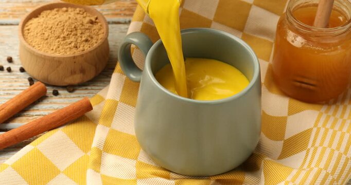 Golden milk turmeric latte. Pouring drink into cup at old wooden table, closeup